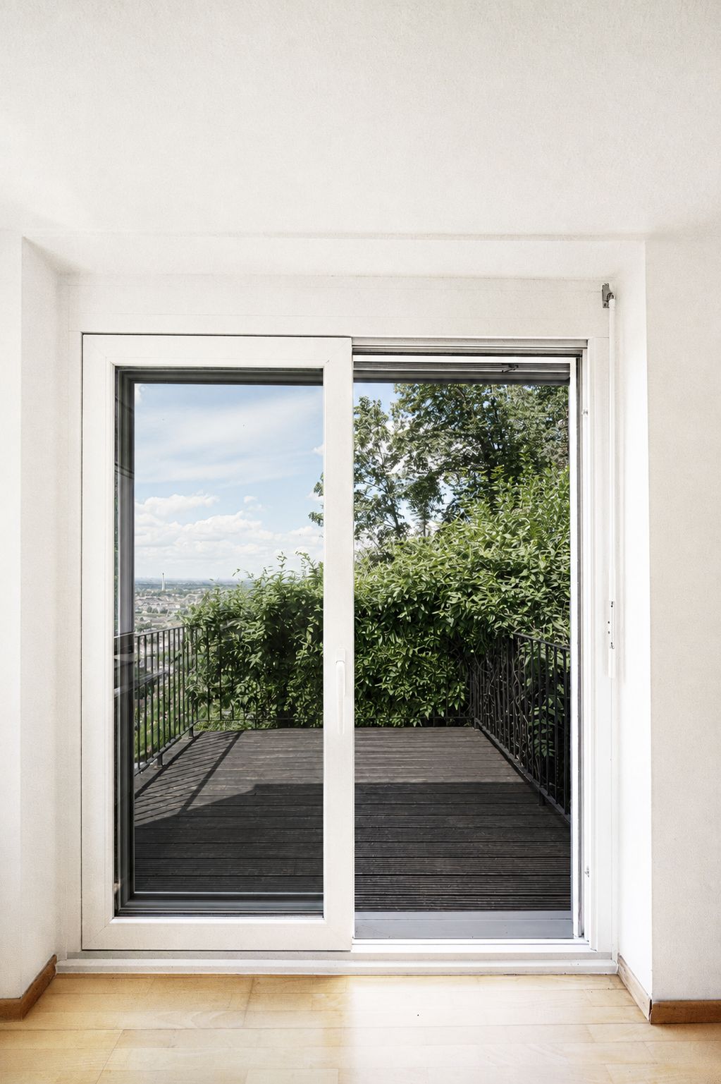 Große Glasschiebetür mit Blick auf eine Terrasse und grüne Büsche draußen.
