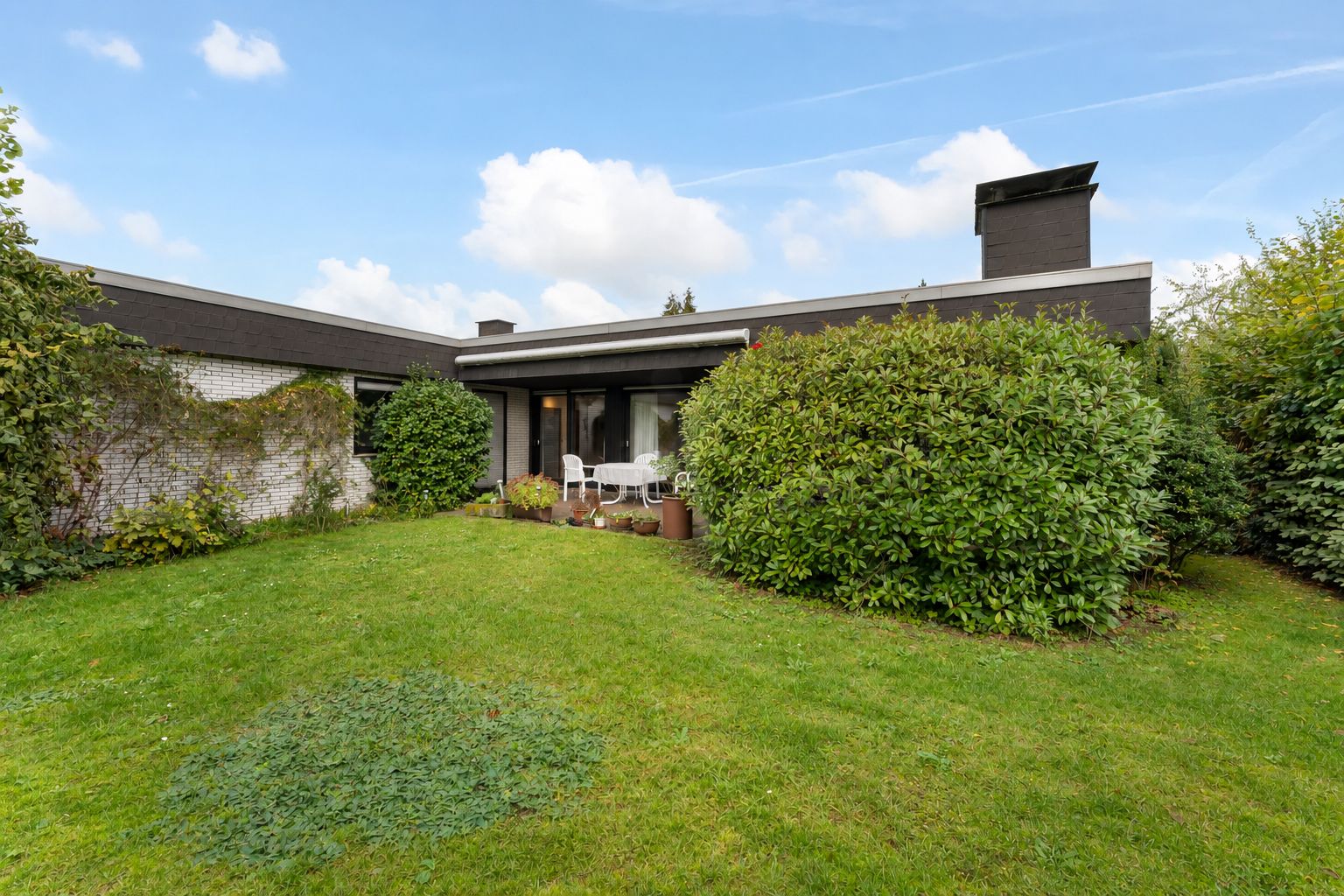 Einfamilienhaus mit Flachdach, Terrasse, Gartenmöbeln und viel Grün im Garten.