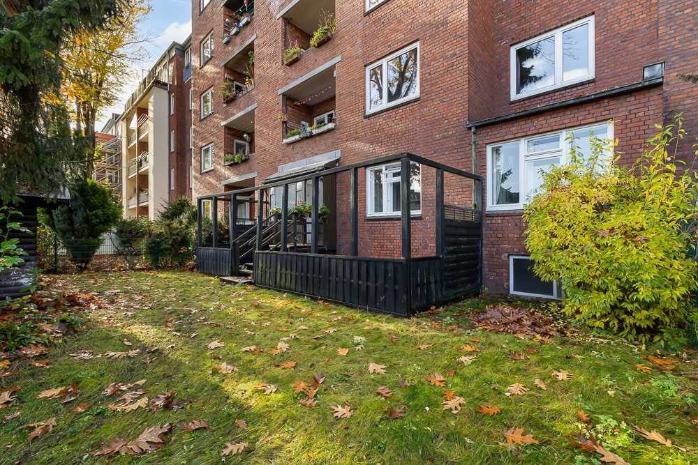 Backsteinwohnhaus mit Holzbalkon und Garten, Herbstlaub auf dem Rasen.