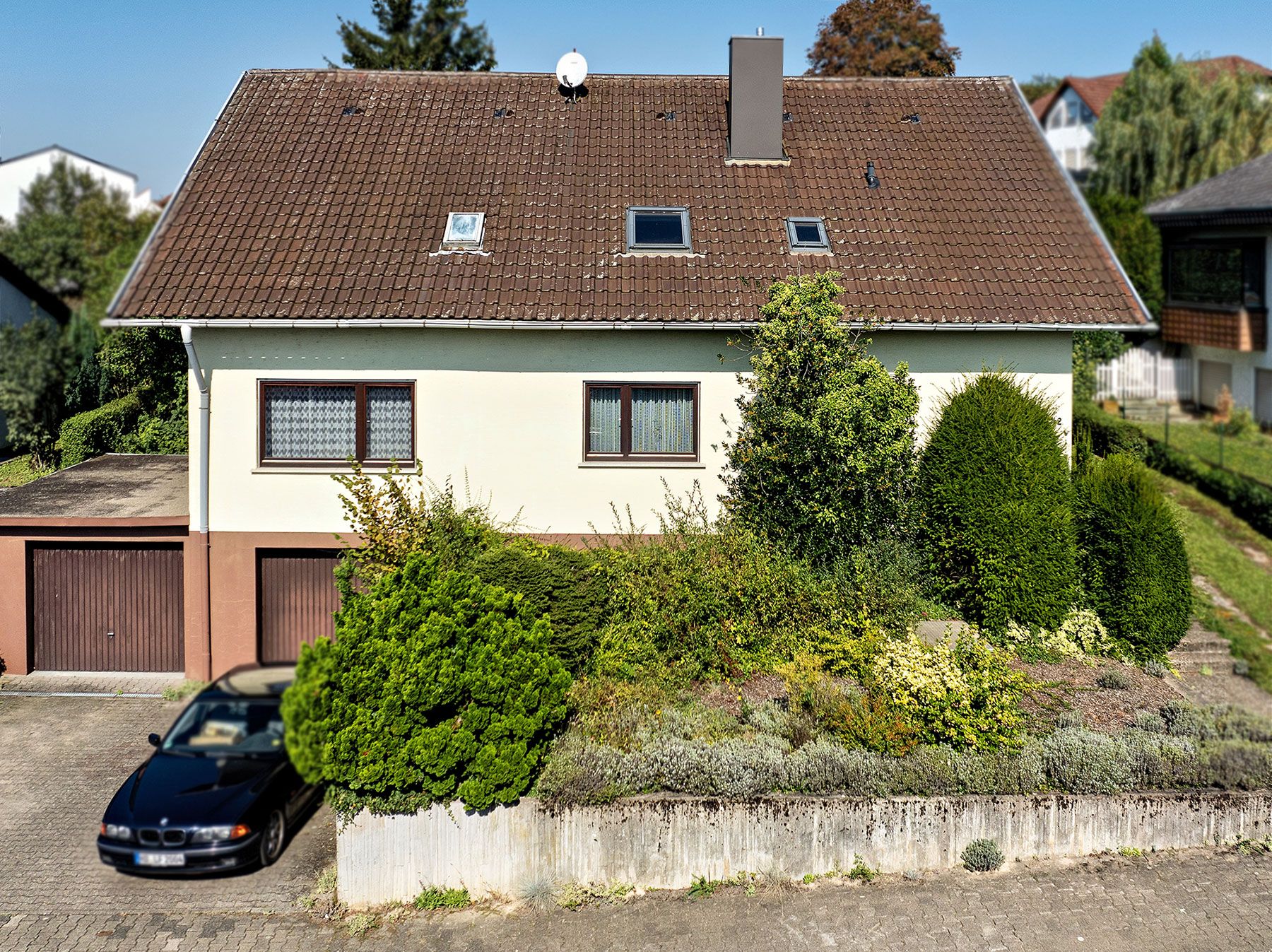 Zweistöckiges Wohnhaus mit Garten, Garage und schwarzem Auto davor.