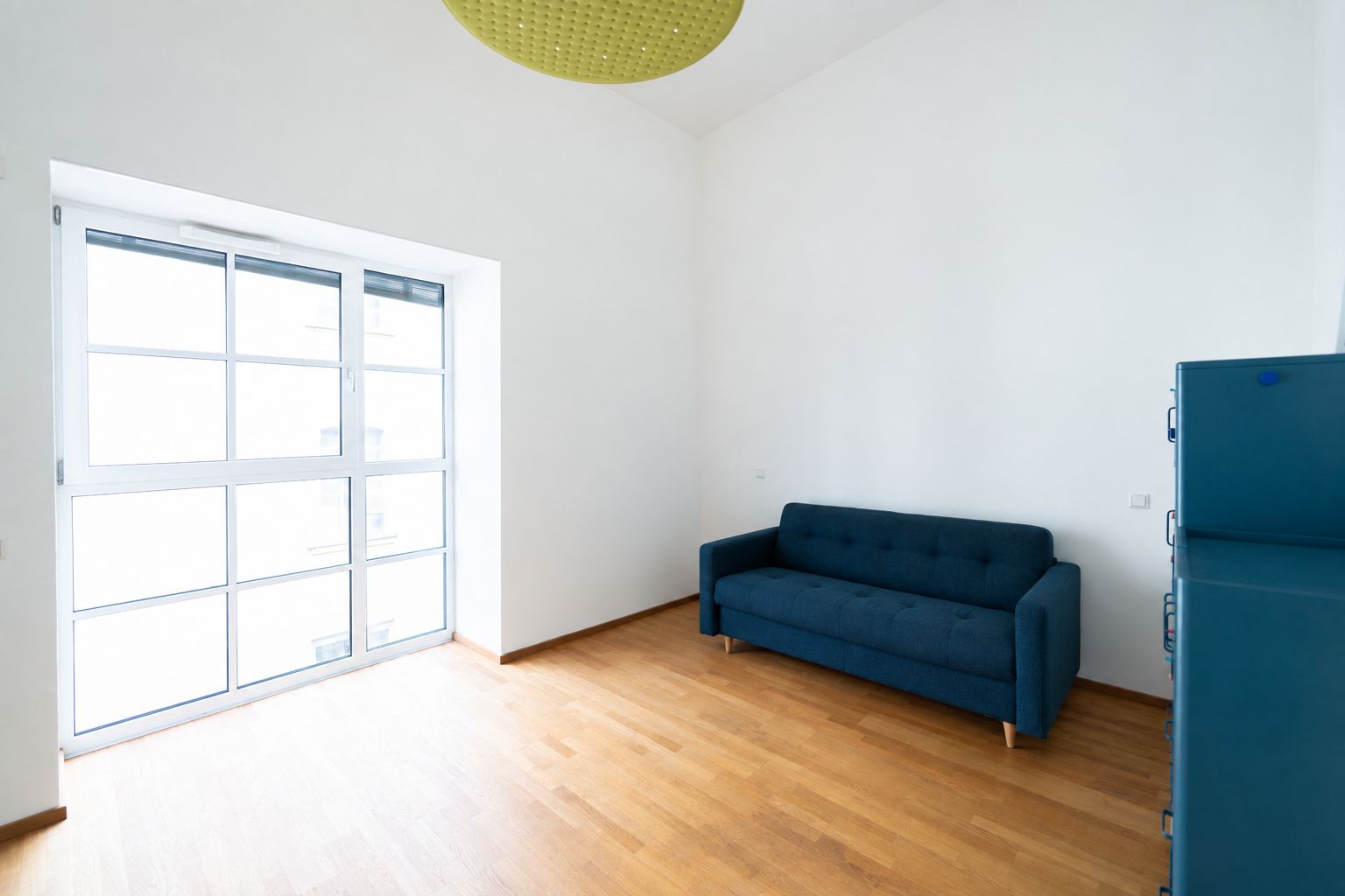 Helles Zimmer mit Holzboden, großer Fensterfront und dunkelblauem Sofa.