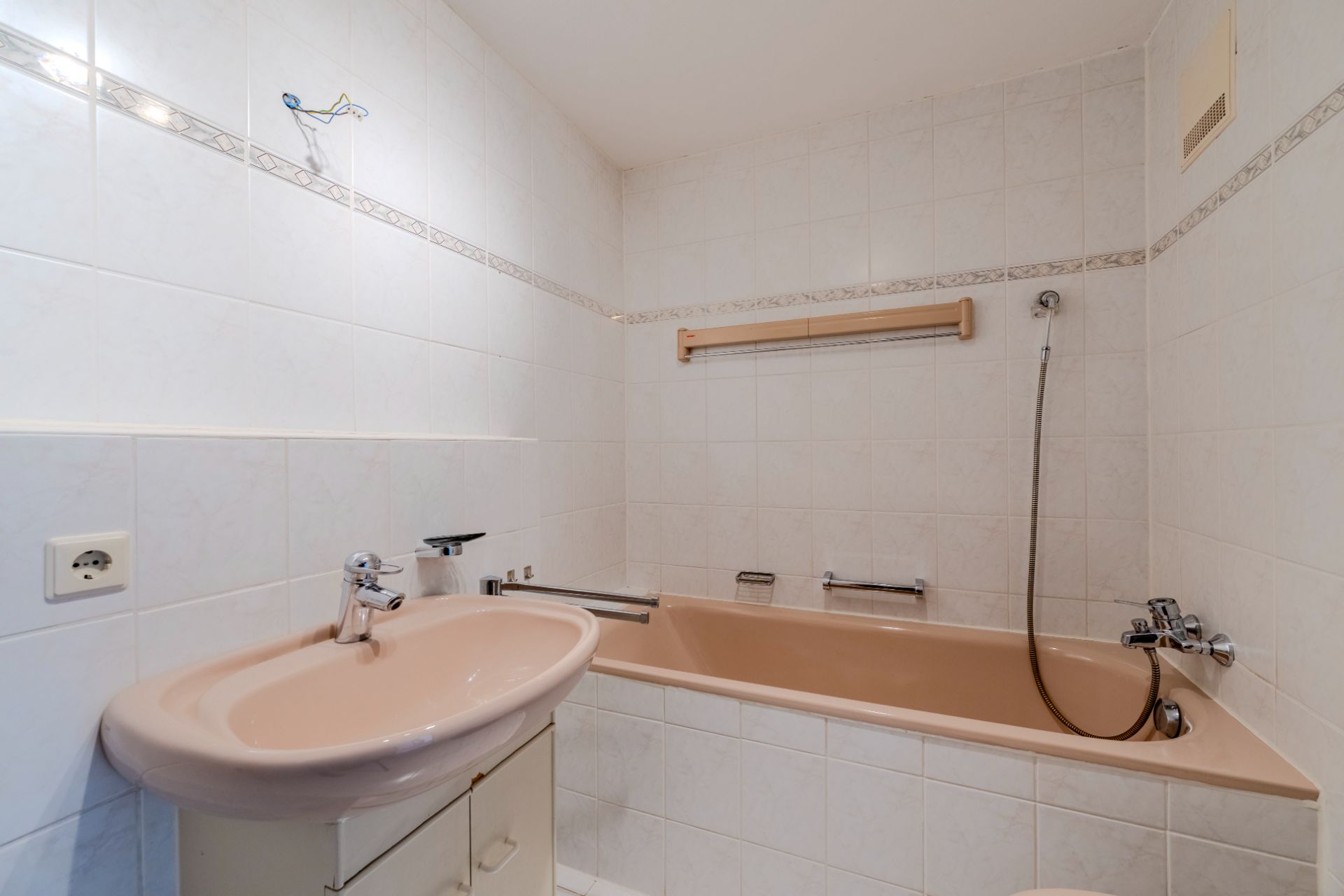 Badezimmer mit beiger Badewanne, Waschbecken und weißen Fliesen an den Wänden.