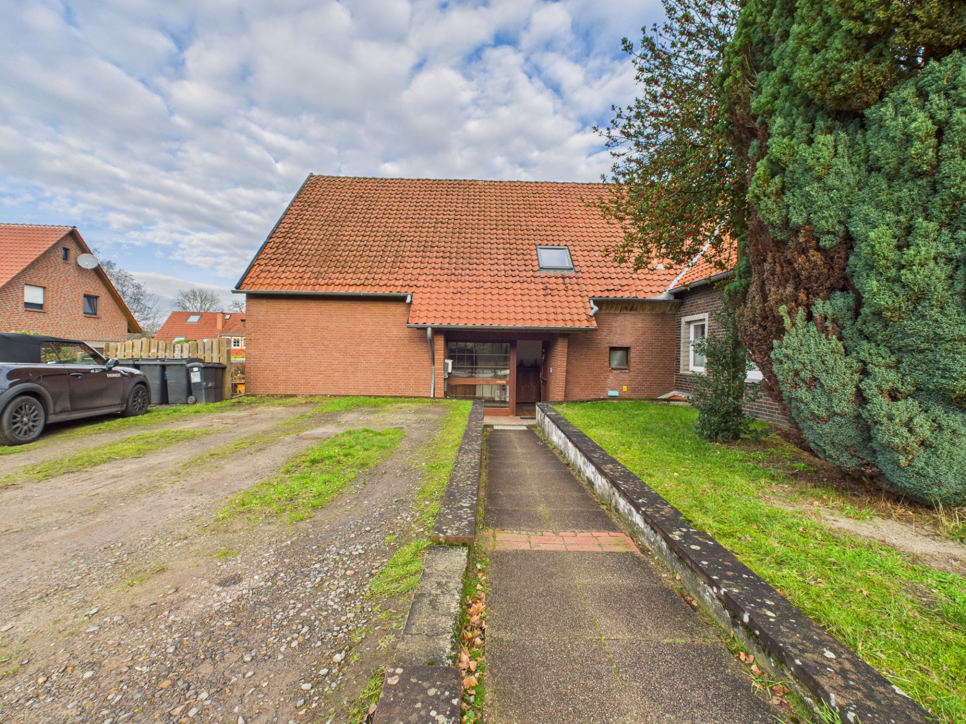 Einfamilienhaus mit rotem Dach, Einfahrt und Gehweg, großer Baum rechts im Vorgarten.
