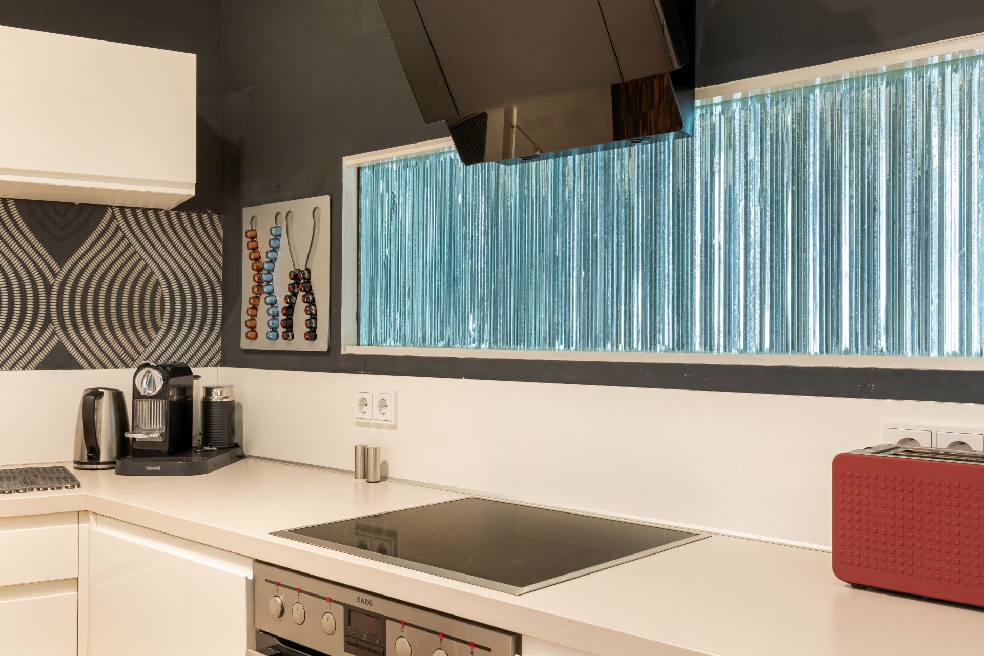 Moderne Küche mit Herd, Kaffeemaschine, Toaster und großem Fenster mit blauen Glasbausteinen.