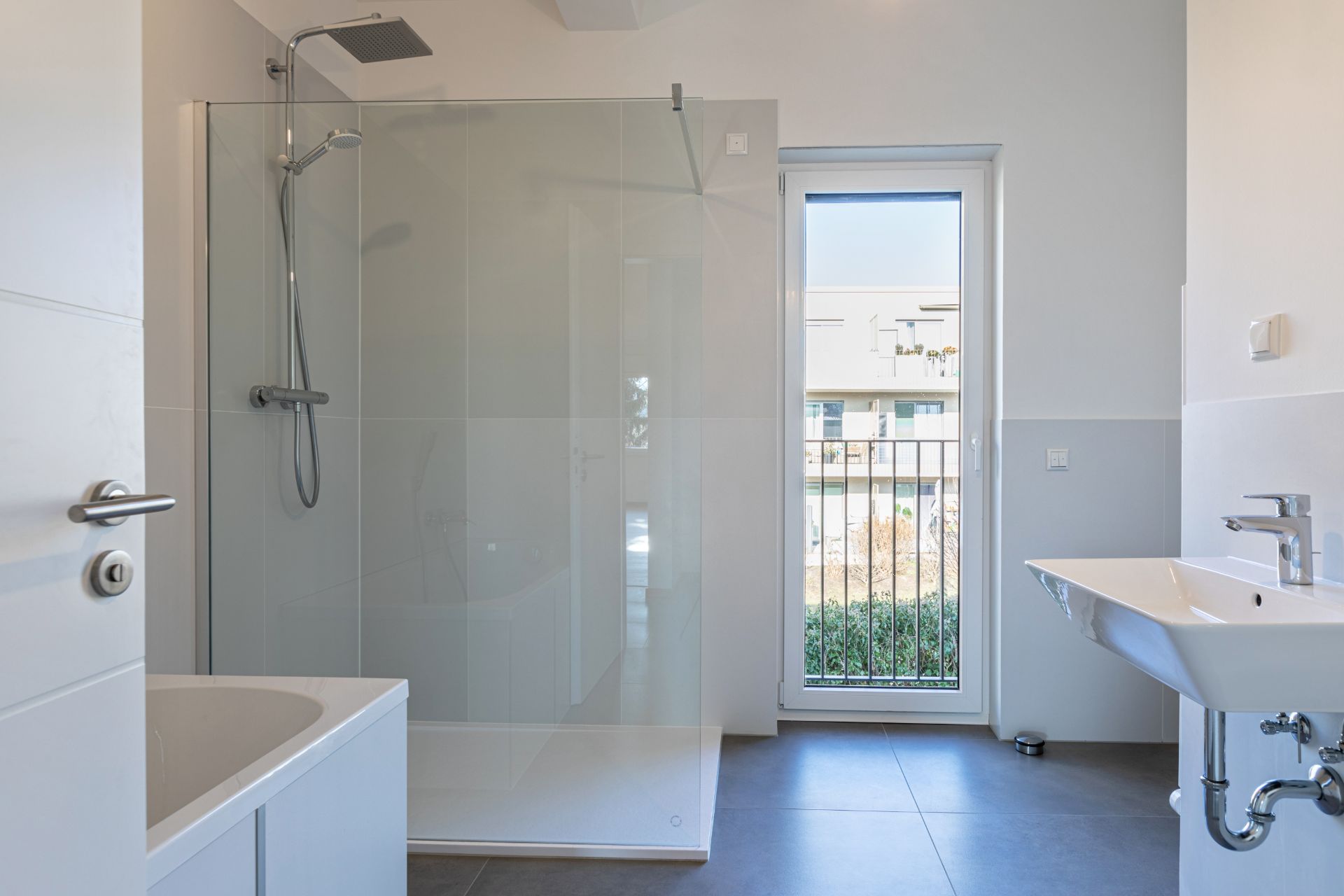 Modernes Badezimmer mit ebenerdiger Dusche, Badewanne, Waschbecken und Fenster mit Blick nach draußen.