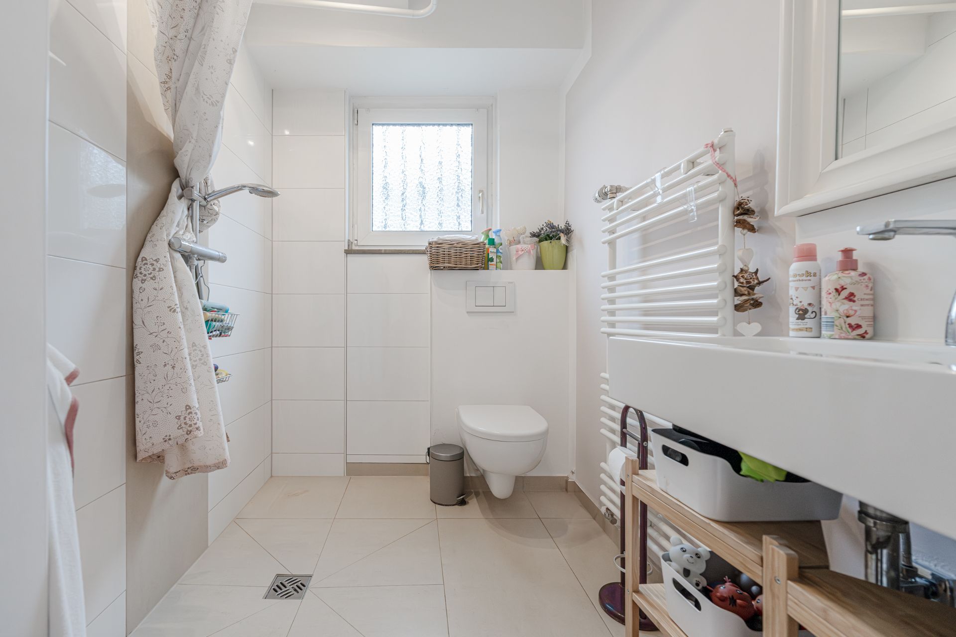 Modernes Badezimmer mit Dusche, WC, Waschbecken und Fenster, hell und ordentlich eingerichtet.