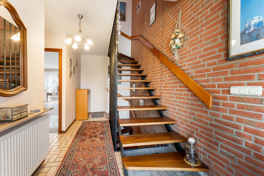 Flur mit Teppichläufer, Spiegel, offener Holztreppe und Backsteinwand.
