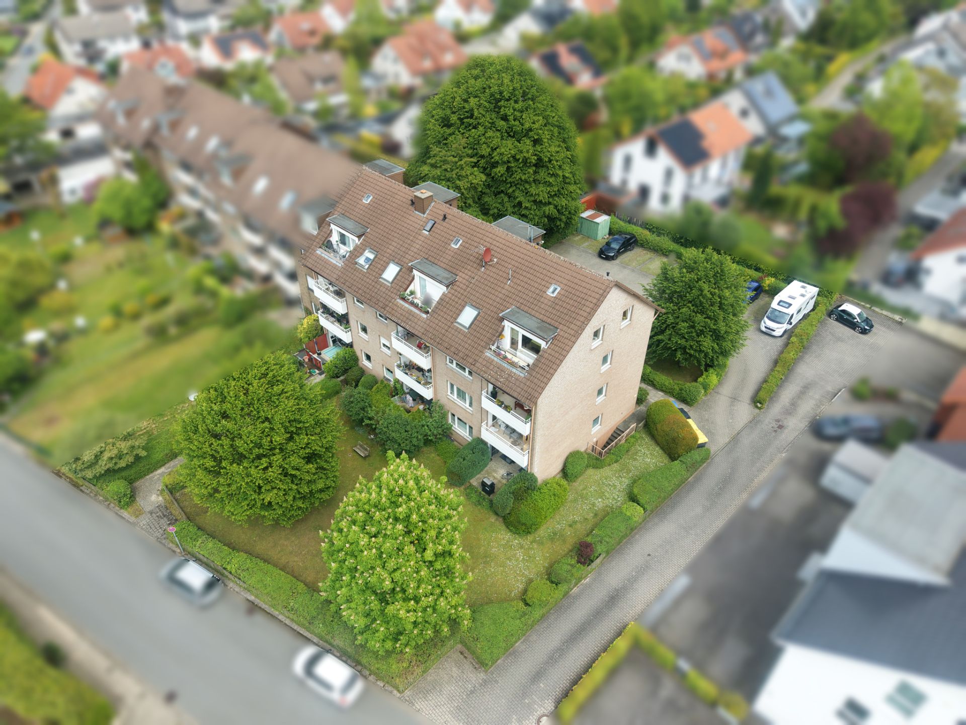 Luftaufnahme eines Wohnhauses mit Garten, Bäumen und angrenzender Straße.