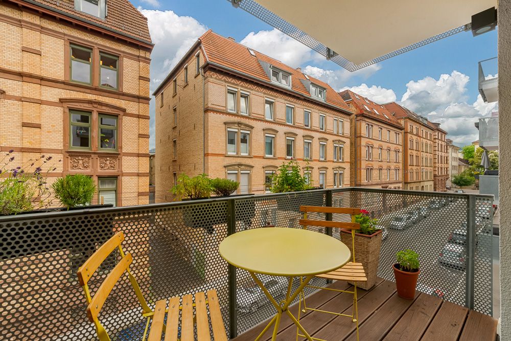 Balkon mit gelbem Tisch, zwei Stühlen und Blick auf Wohnhäuser und eine Straße.