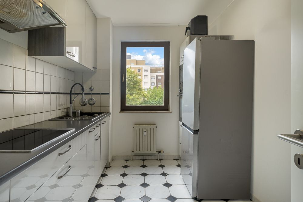 Schmale Küche mit weißen Schränken, großem Fenster und Fliesenboden.