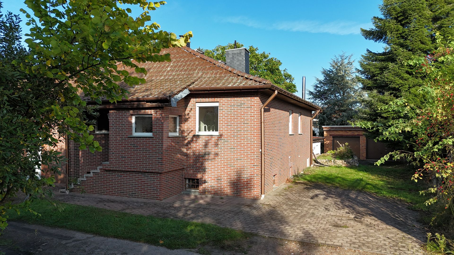 Backsteinhaus mit Satteldach, gepflastertem Weg und umliegenden Bäumen bei Tageslicht.