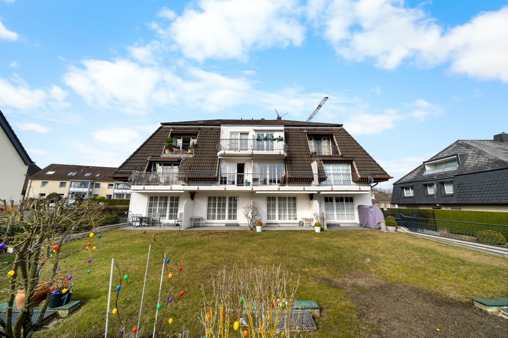 Mehrfamilienhaus mit Balkon und großem Garten, bunte Dekoration im Vordergrund.