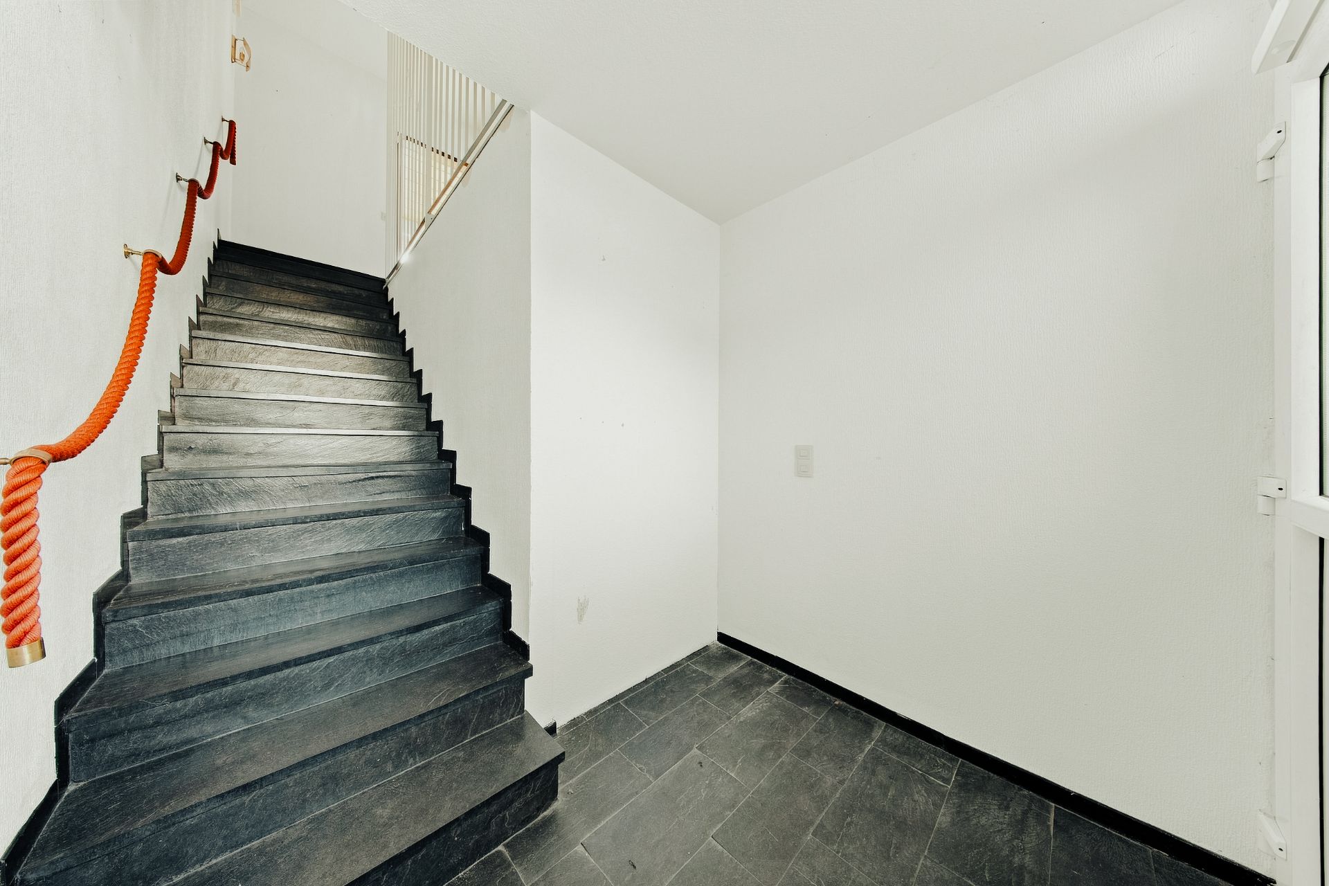 Heller Flur mit schwarzer Treppe und rotem Seil als Handlauf.