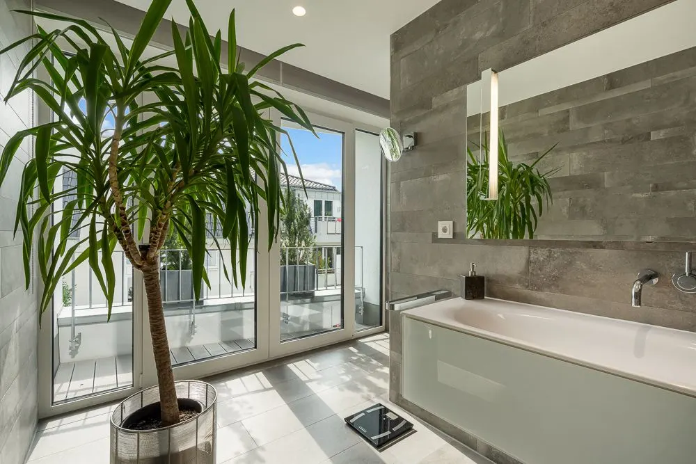 Modernes Badezimmer mit großer Pflanze, Badewanne und Fensterfront zur Terrasse.