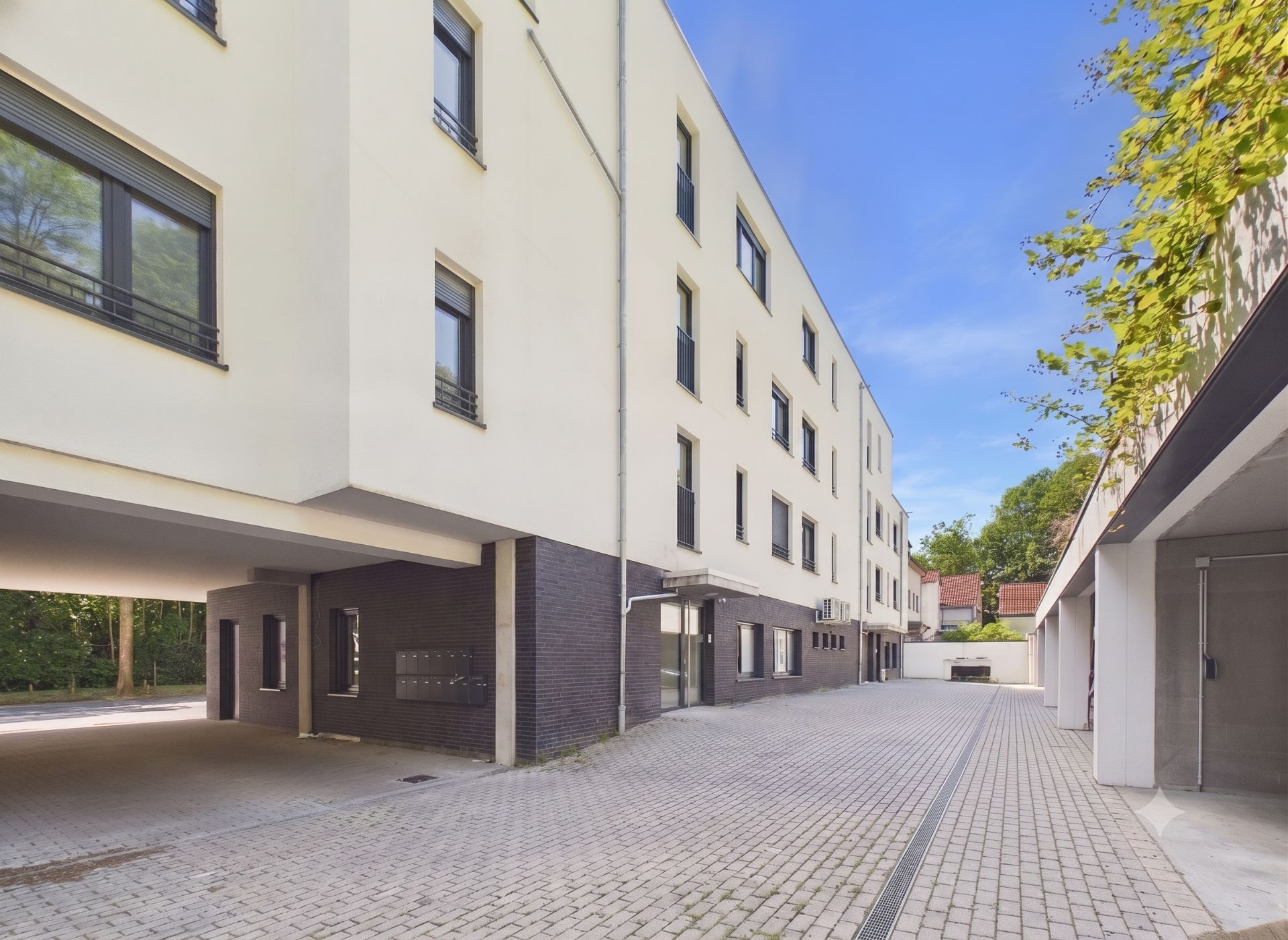 Moderner Wohnhauskomplex mit gelber Fassade und gepflastertem Innenhof an einem sonnigen Tag.