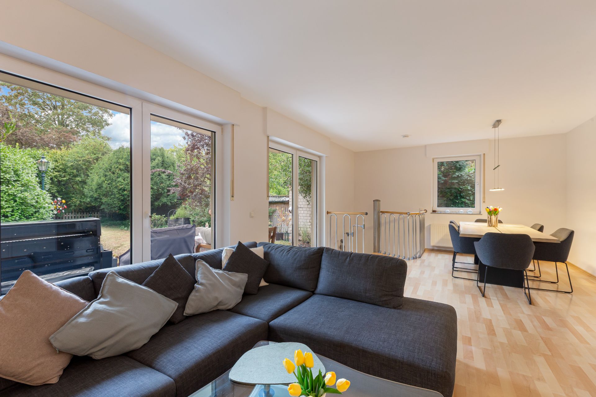 Wohnzimmer mit großer Eckcouch, Esstisch, großen Fenstern und Blick in den Garten.