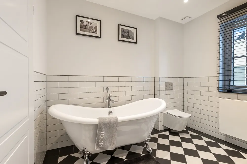 Modernes Badezimmer mit freistehender Badewanne, Wandtoilette und schwarz-weiß kariertem Boden.