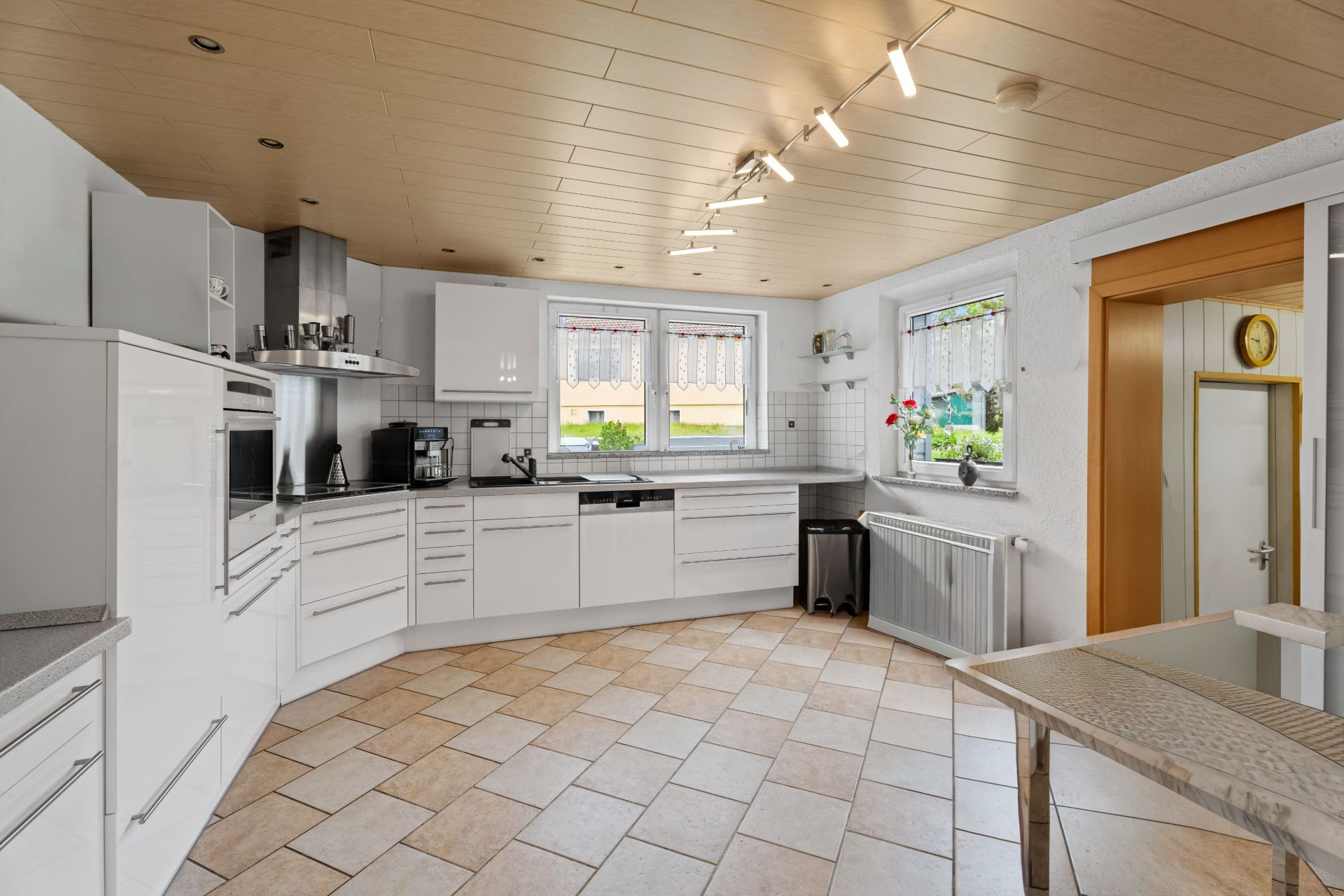 Moderne helle Küche mit weißen Schränken, zwei Fenstern und Esstisch.