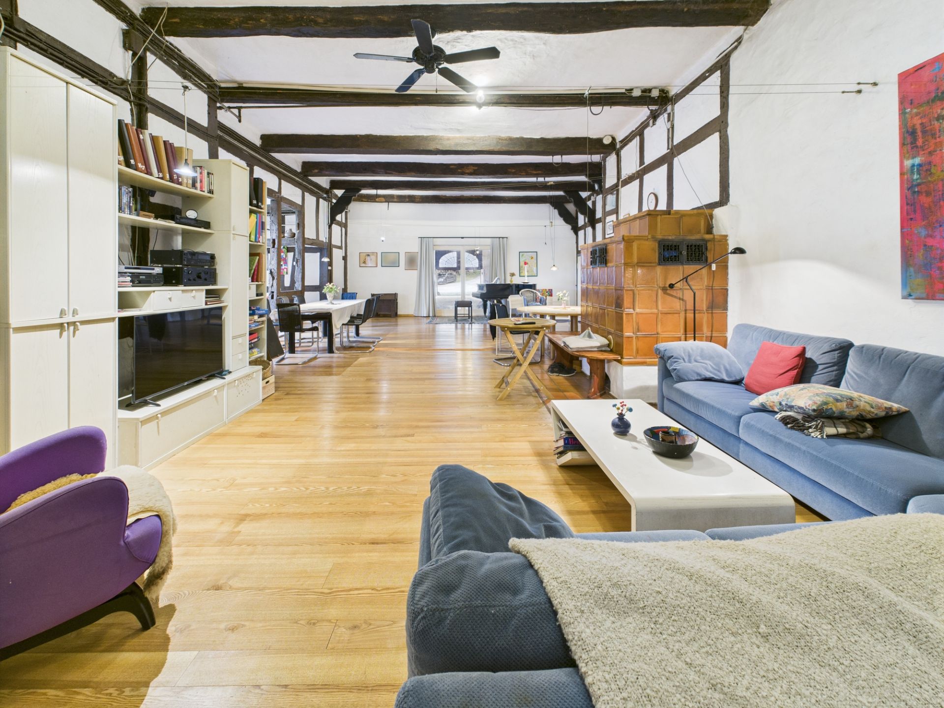 Großes, offen gestaltetes Wohnzimmer mit Holzboden, Deckenbalken, Sofa, Regal und Esstisch.