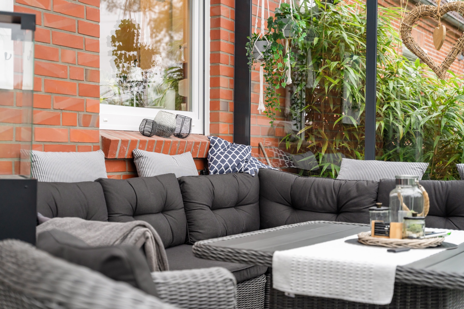 Gemütliche Sitzecke mit grauem Sofa und Tisch auf einer Terrasse mit grünen Pflanzen.