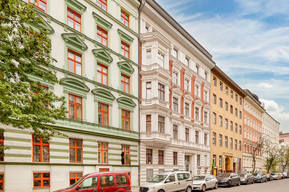 Mehrere mehrstöckige Wohnhäuser an einer ruhigen Straße mit parkenden Autos.