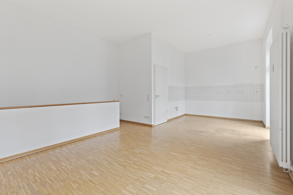 Leerer Raum mit Holzfußboden, weißen Wänden und Fliesen an einer Wand.