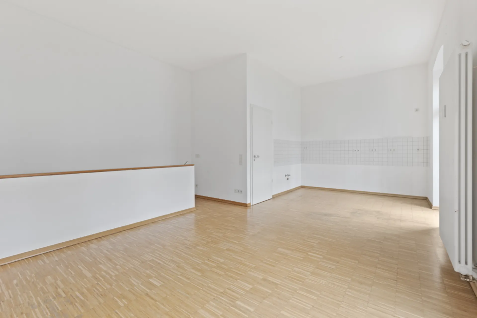 Leerer Raum mit Holzfußboden, weißen Wänden und Fliesen an einer Wand.
