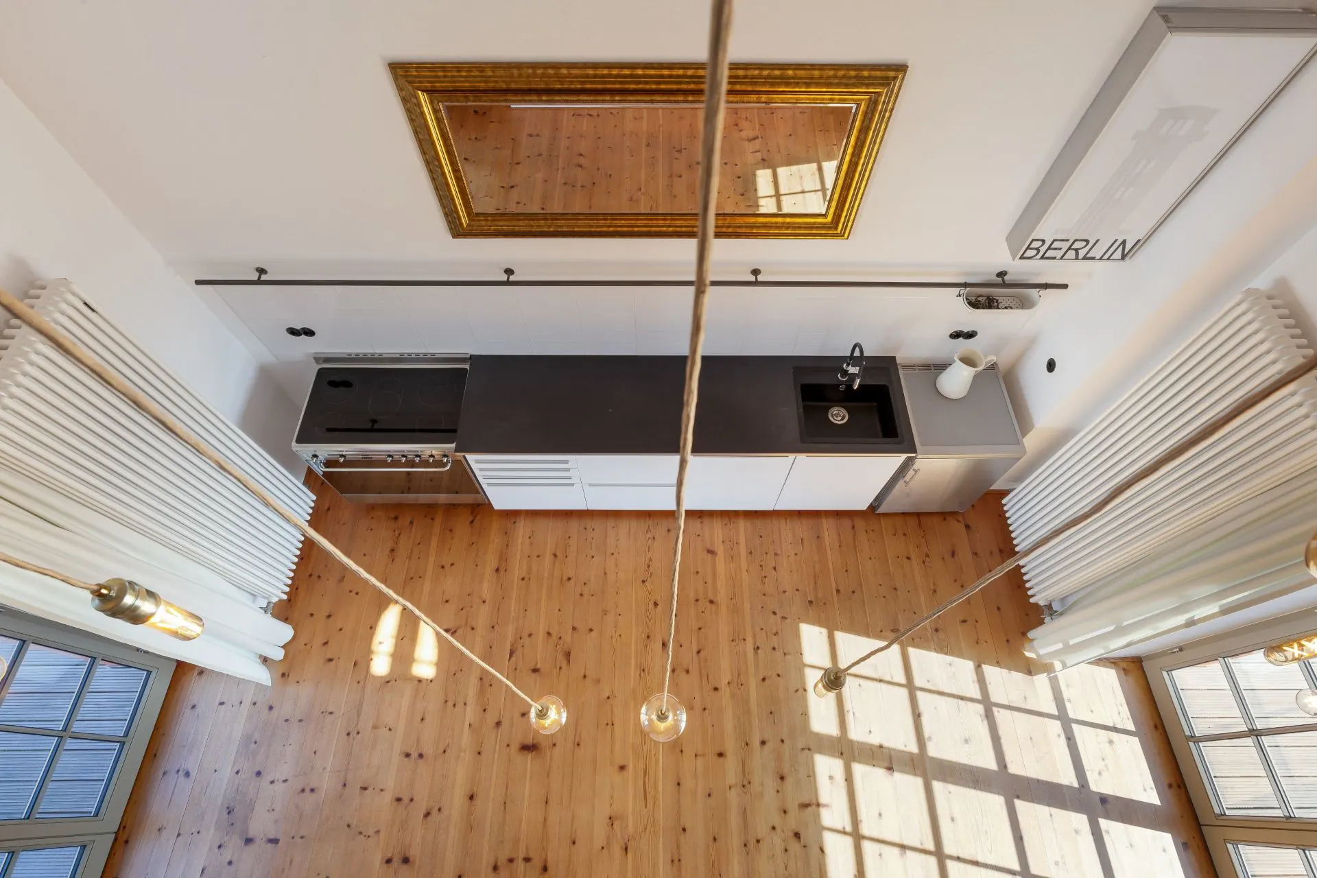 Moderne Küche mit schwarzen Arbeitsflächen und Holzfußboden, von oben fotografiert.