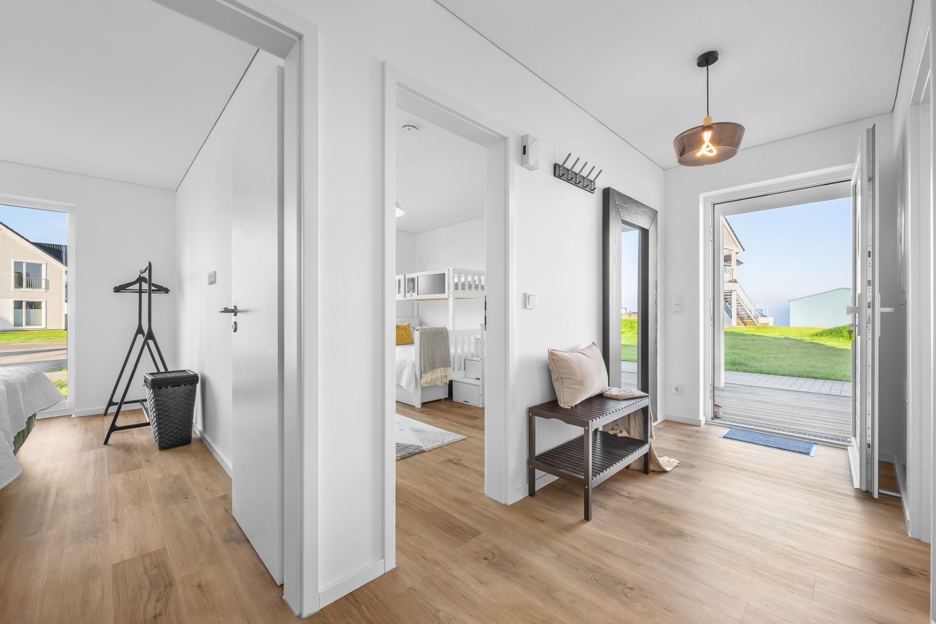 Heller Flur mit Holzfußboden, offenen Türen zu Schlafzimmern und Blick auf eine Terrasse mit Garten.