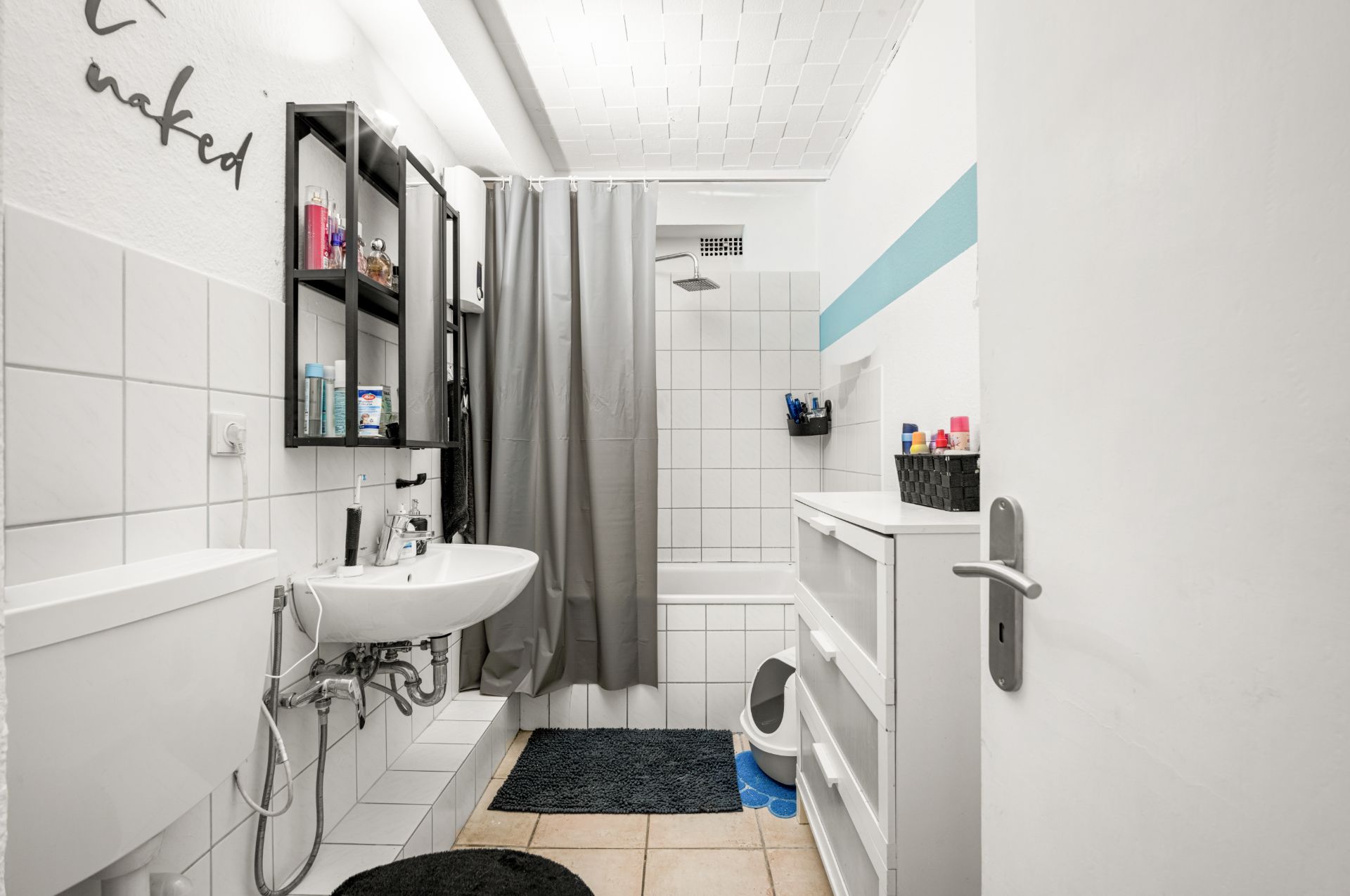 Helles Badezimmer mit Waschbecken, Spiegel, Badewanne mit Duschvorhang und weißen Fliesen.