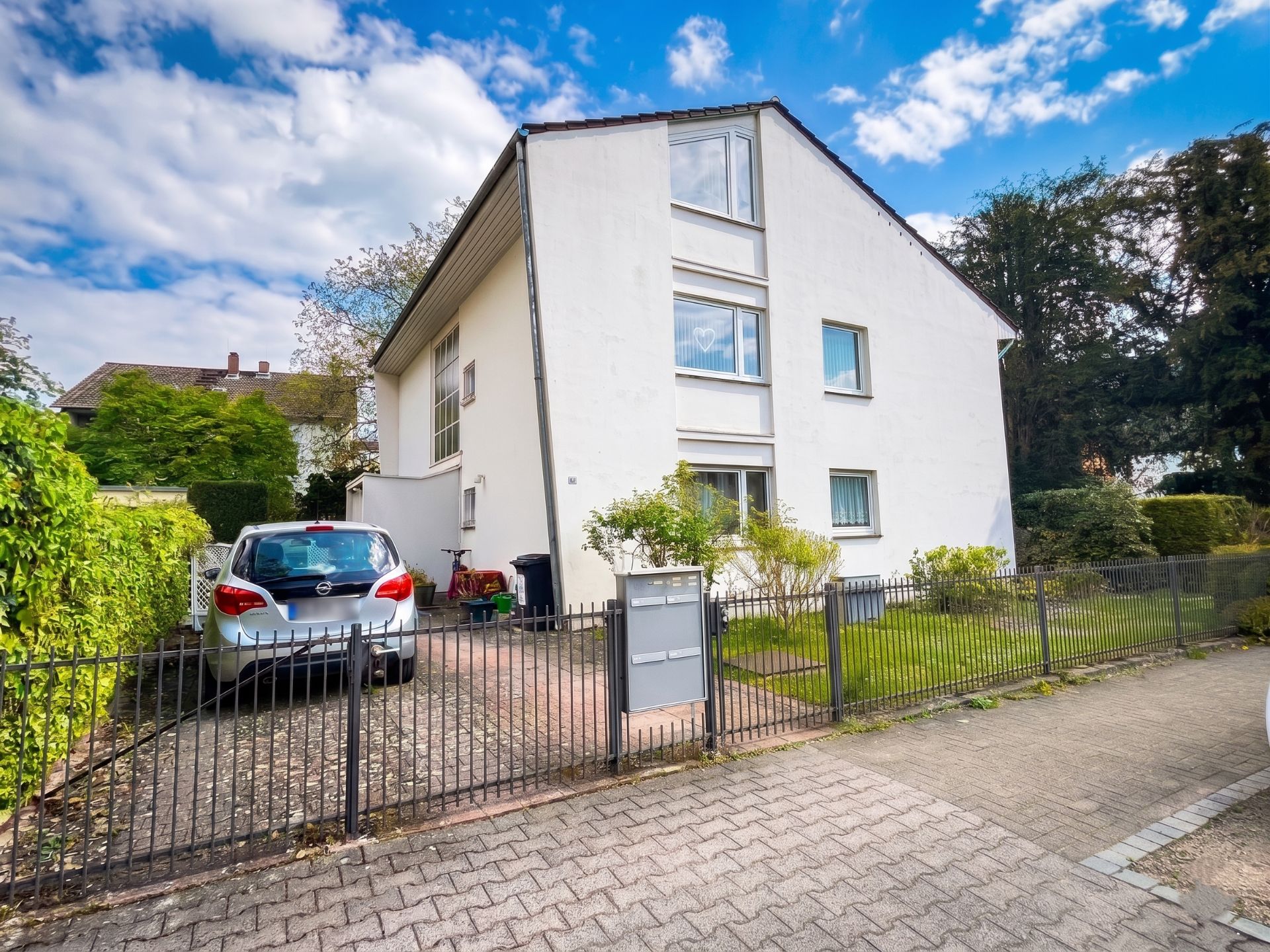 Weißes Wohnhaus mit Garten, Zaun und geparktem Auto auf dem Grundstück.