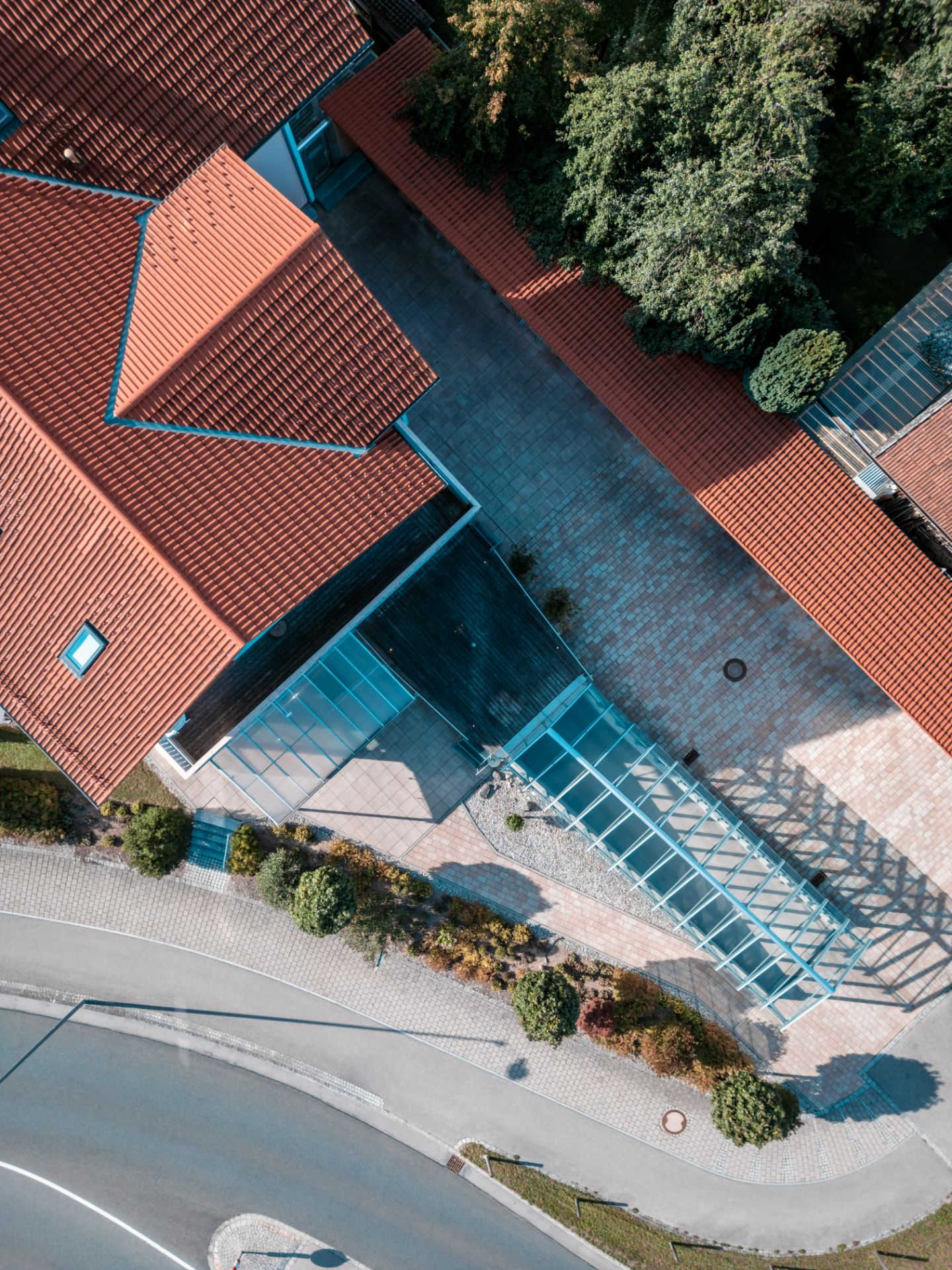 Luftaufnahme eines Wohnhauses mit rotem Dach, Glasüberdachung und umliegendem Garten.