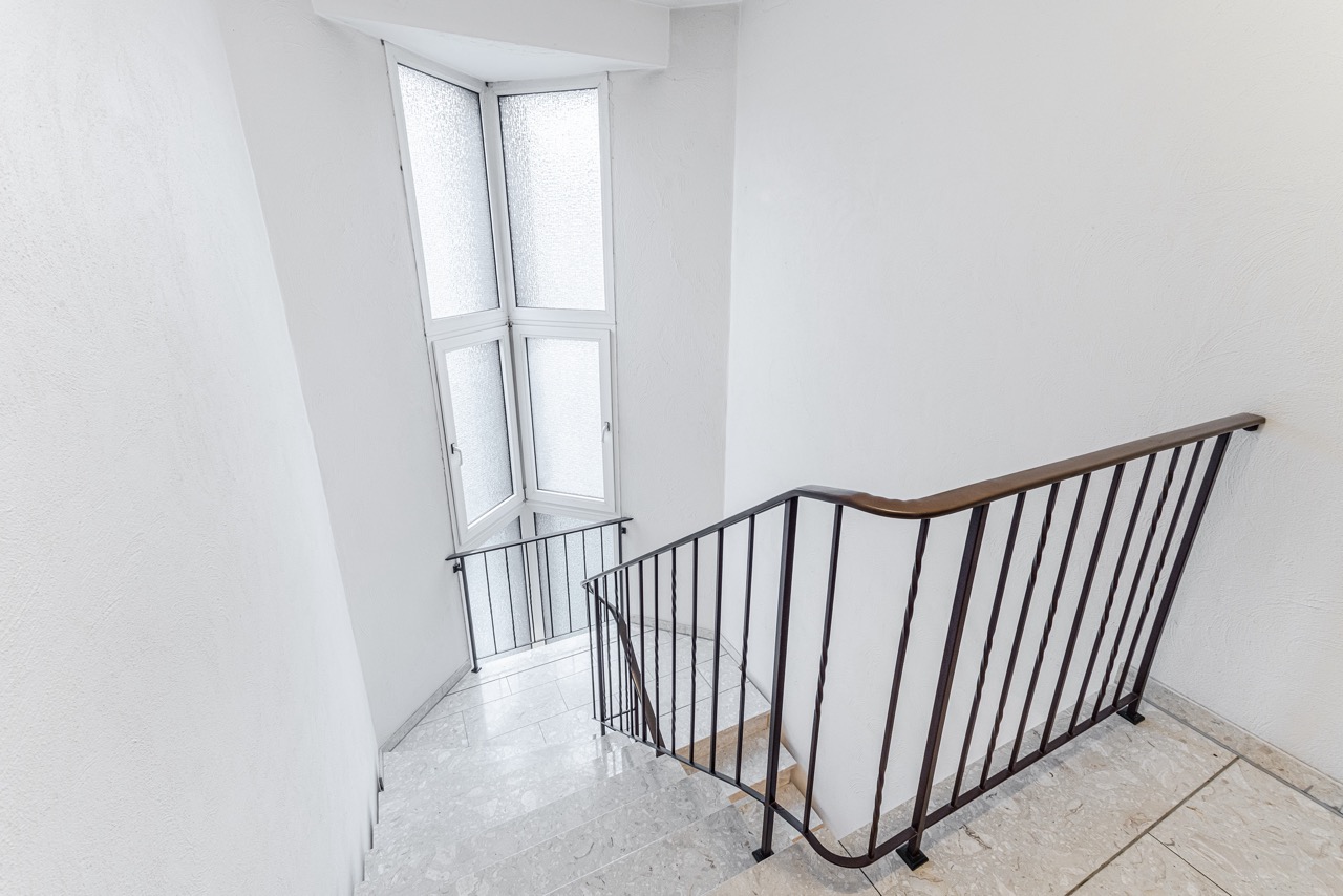 Helle Treppe mit Metallgeländer und großem Fenster mit Milchglas.