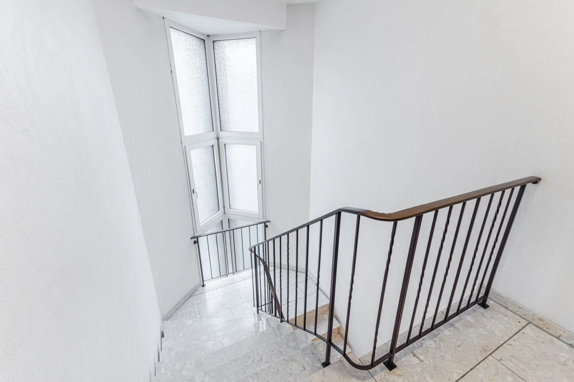 Helle Treppe mit Metallgeländer und großem Fenster mit Milchglas.