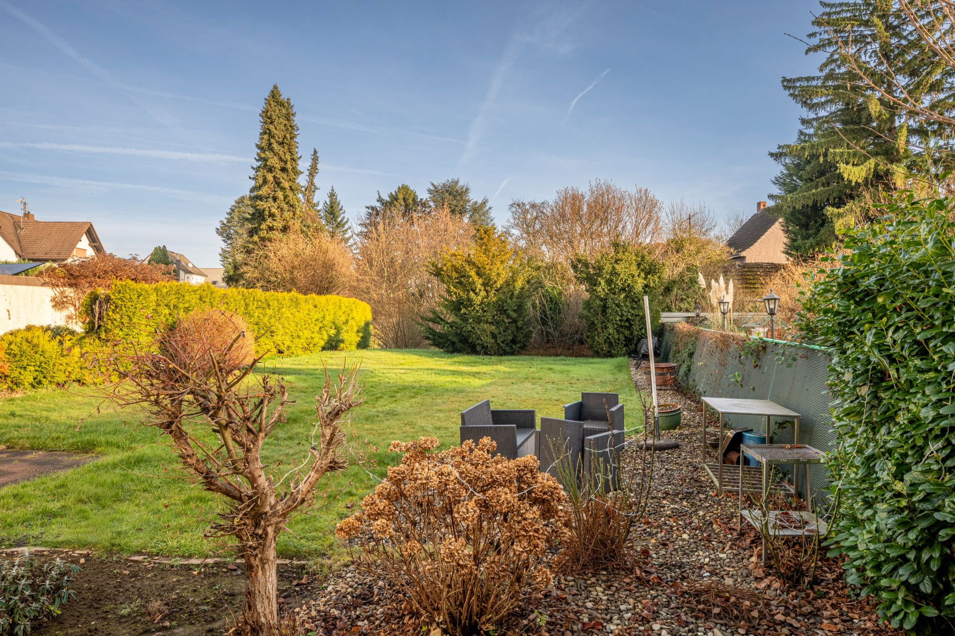 Großer Garten mit Rasenfläche, Sträuchern, Gartenmöbeln und Sicht auf Nachbarhäuser.