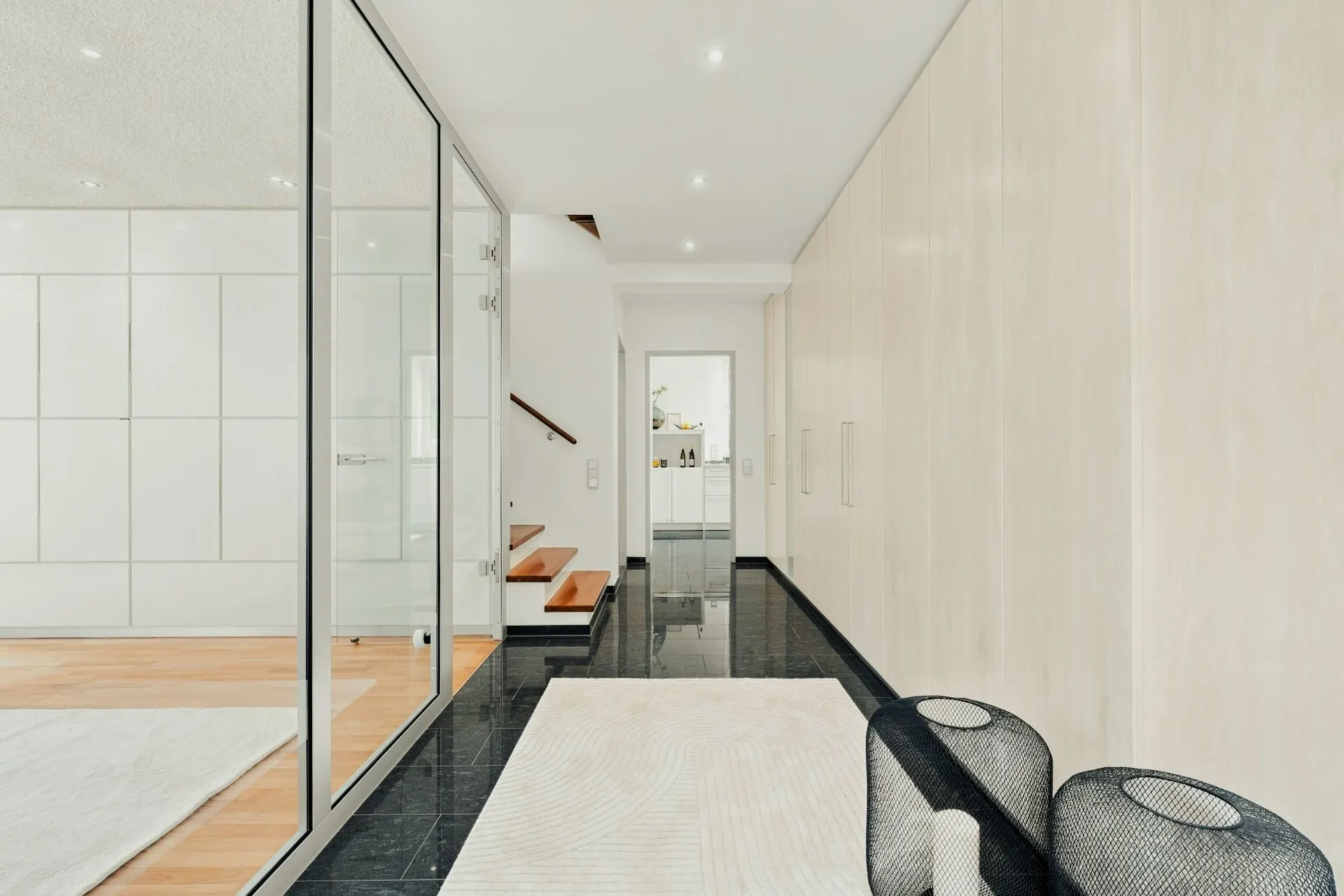 Moderner Flur mit dunklem Boden, hellem Teppich und Glastrennwand, links eine Treppe.