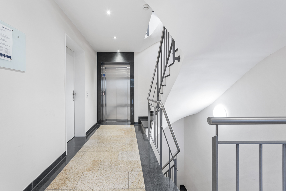 Heller Flur mit Aufzug, Treppe und weiß gestrichenen Wänden in einem Wohngebäude.