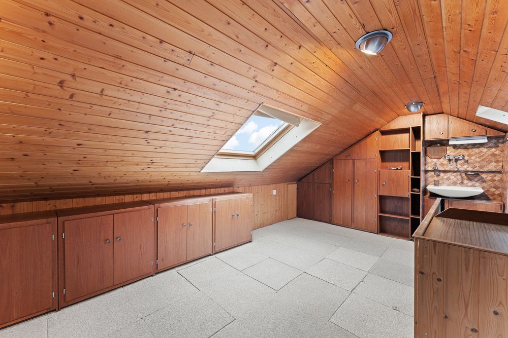 Dachzimmer mit Holzverkleidung, Einbauschränken, Dachfenster und kleinem Waschbecken.