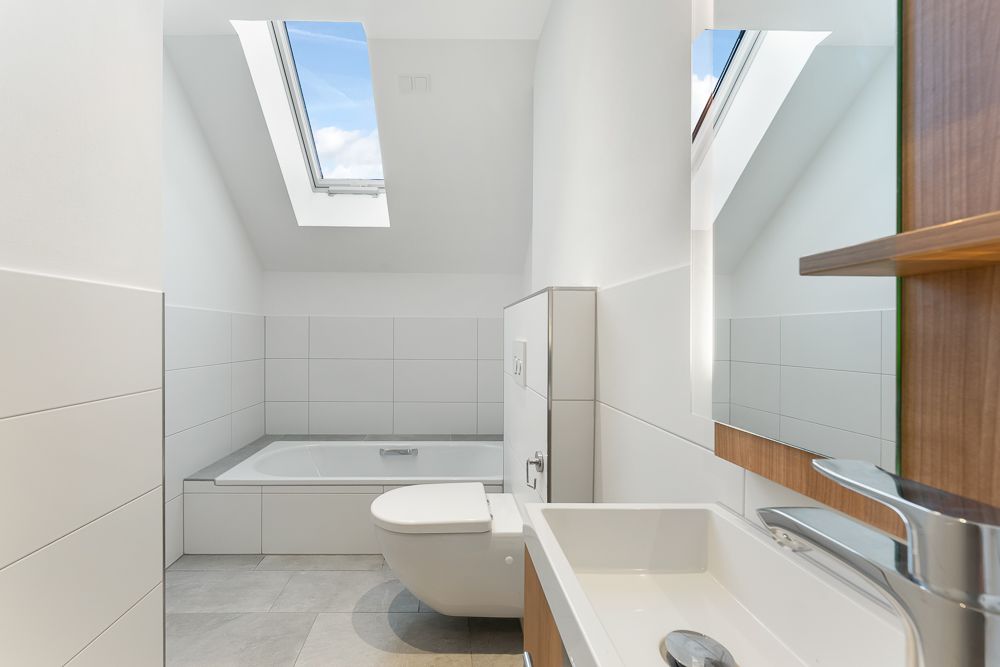 Modernes Bad mit Dachfenster, Badewanne, Wandtoilette und Waschbecken.