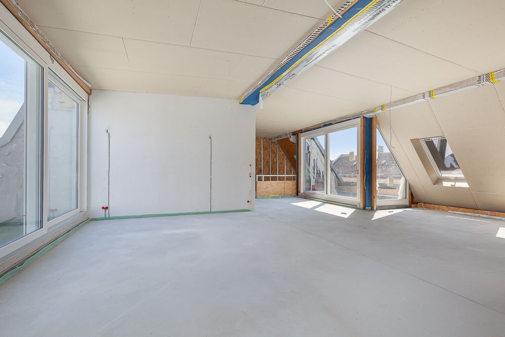 Heller, unfertiger Dachbodenraum mit großen Fenstern und sichtbaren Kabeln an der Decke.