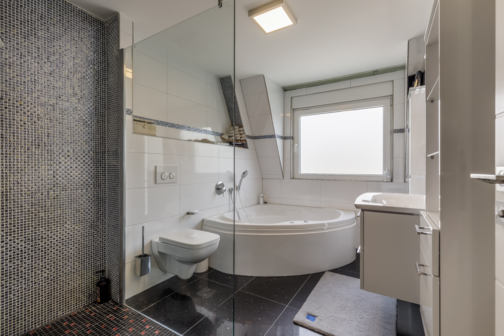 Modernes Badezimmer mit Eckbadewanne, Dusche, WC und großem Fenster.