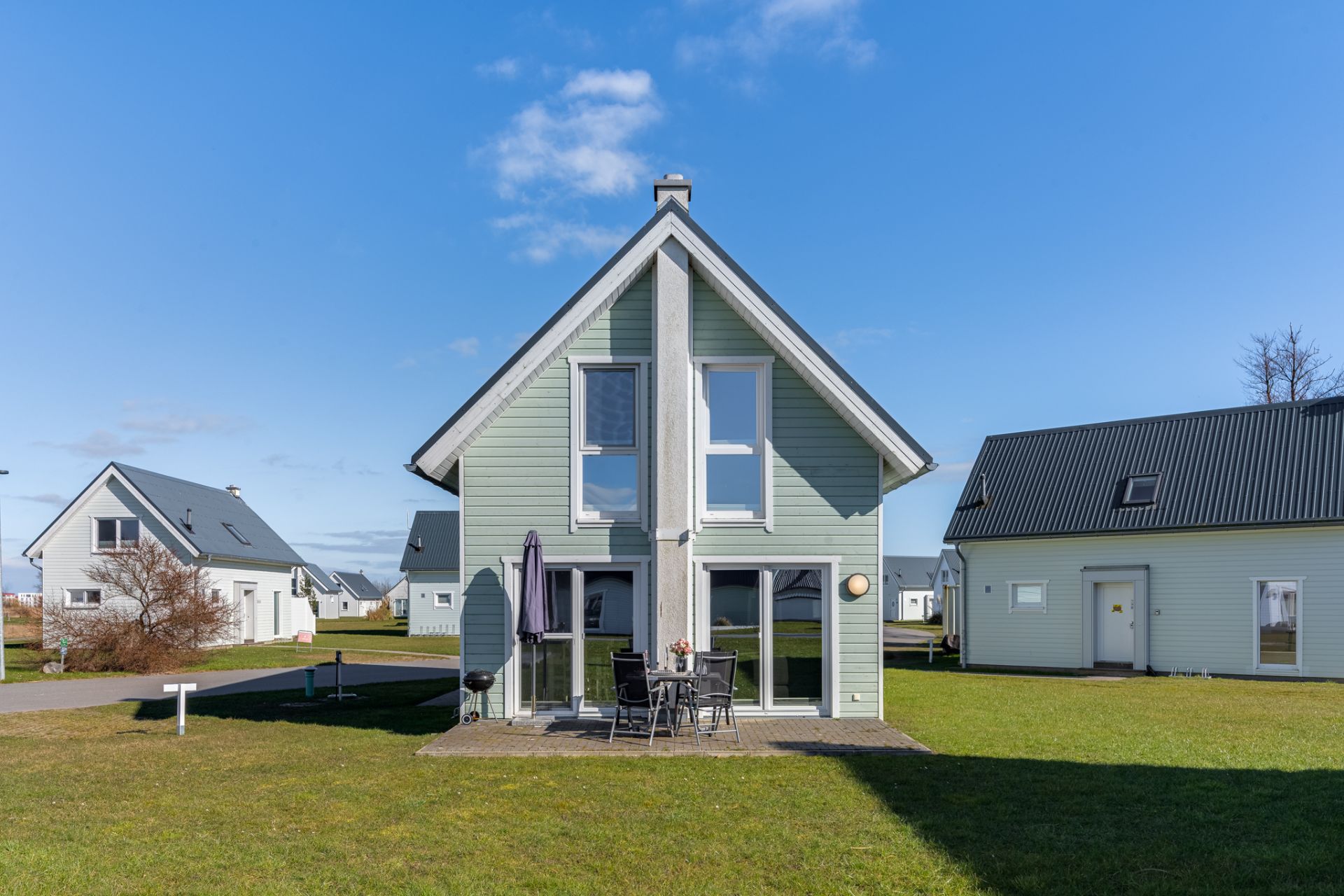 Modernes Einfamilienhaus mit Terrasse, Gartenmöbeln und Sonnenschirm auf grünem Rasen.