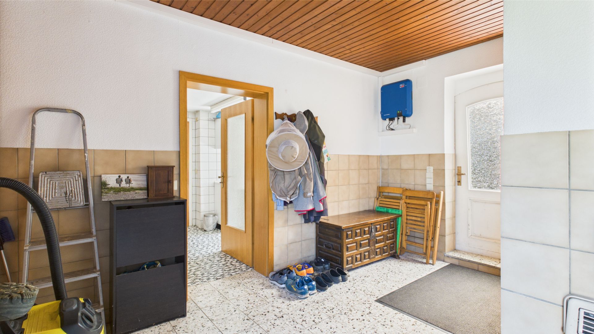 Hausflur mit Garderobe, Schuhen, Regalen, Leiter und Tür zum Badezimmer.