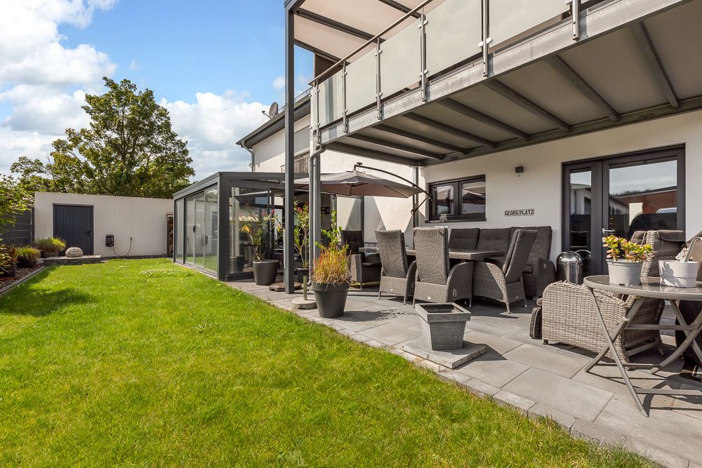Moderne Terrasse mit Sitzmöbeln, Sonnenschirm und Grünfläche im Garten eines Wohnhauses.