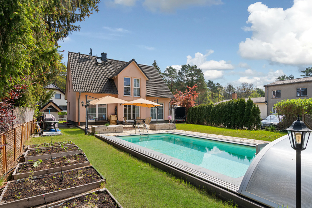 Einfamilienhaus mit Garten, Terrasse, Pool und Hochbeeten bei sonnigem Wetter.