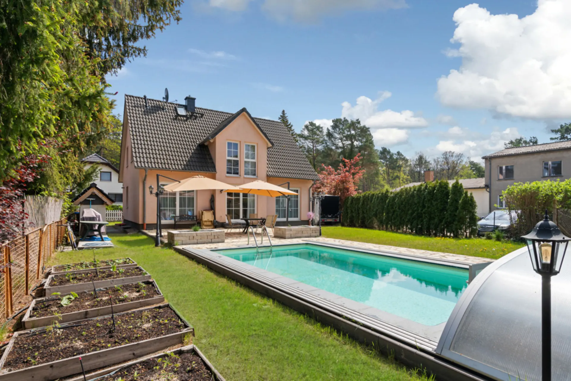 Einfamilienhaus mit Garten, Terrasse, Pool und Hochbeeten bei sonnigem Wetter.
