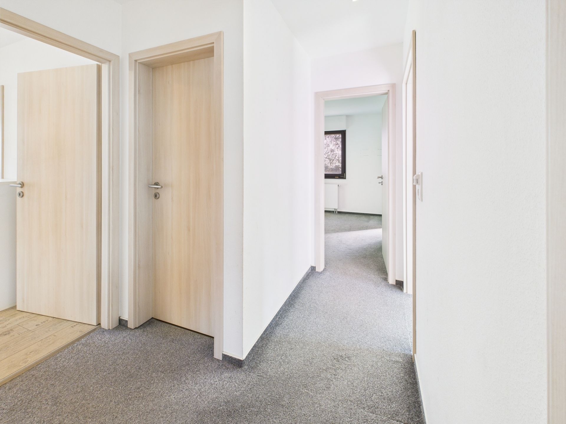Heller Flur mit mehreren Holztüren und grauem Teppichboden in einer Wohnung.