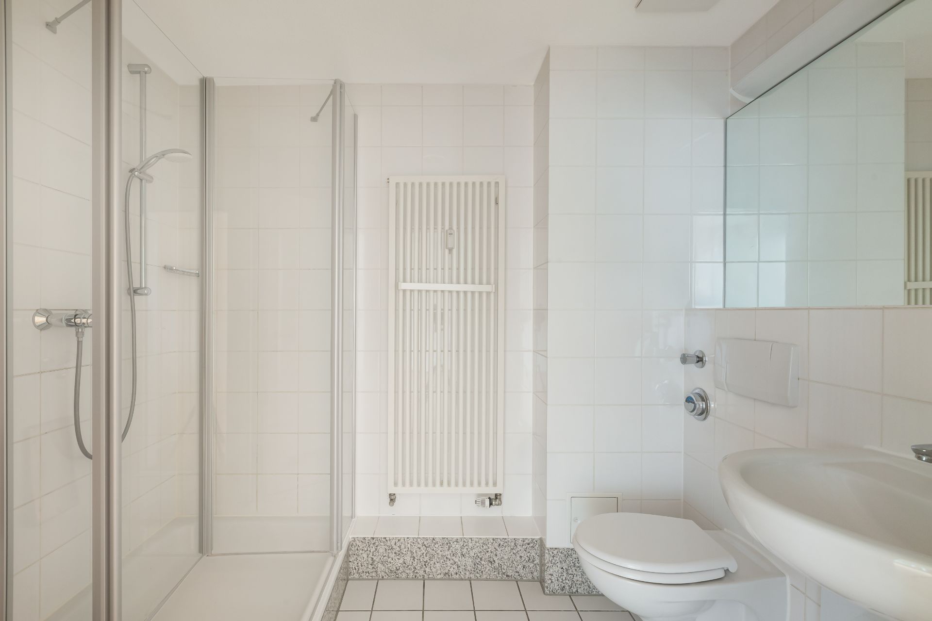 Helles Badezimmer mit Dusche, Wandheizkörper, WC und Waschbecken.
