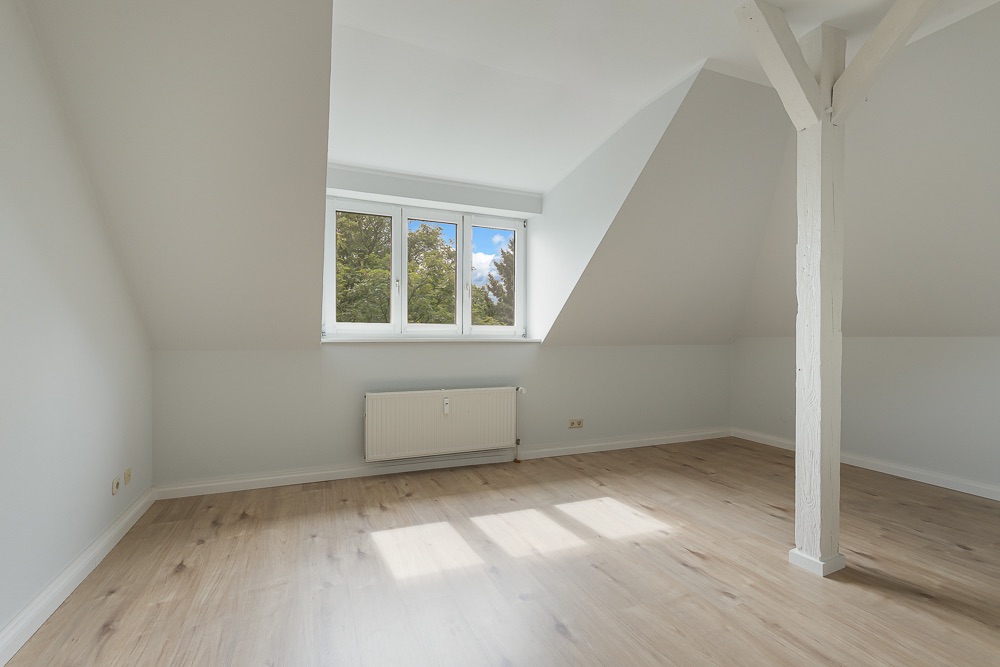 Helles Dachzimmer mit Holzfußboden, großem Fenster und sichtbarem Holzbalken.