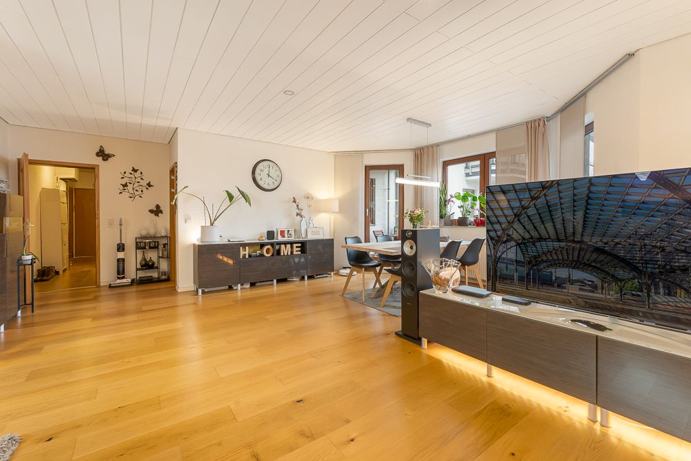 Helles Wohnzimmer mit Holzboden, Esstisch, Fernseher und Dekorationen an der Wand.